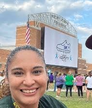 Smiling woman at an outdoor event with a large banner and crowd.
