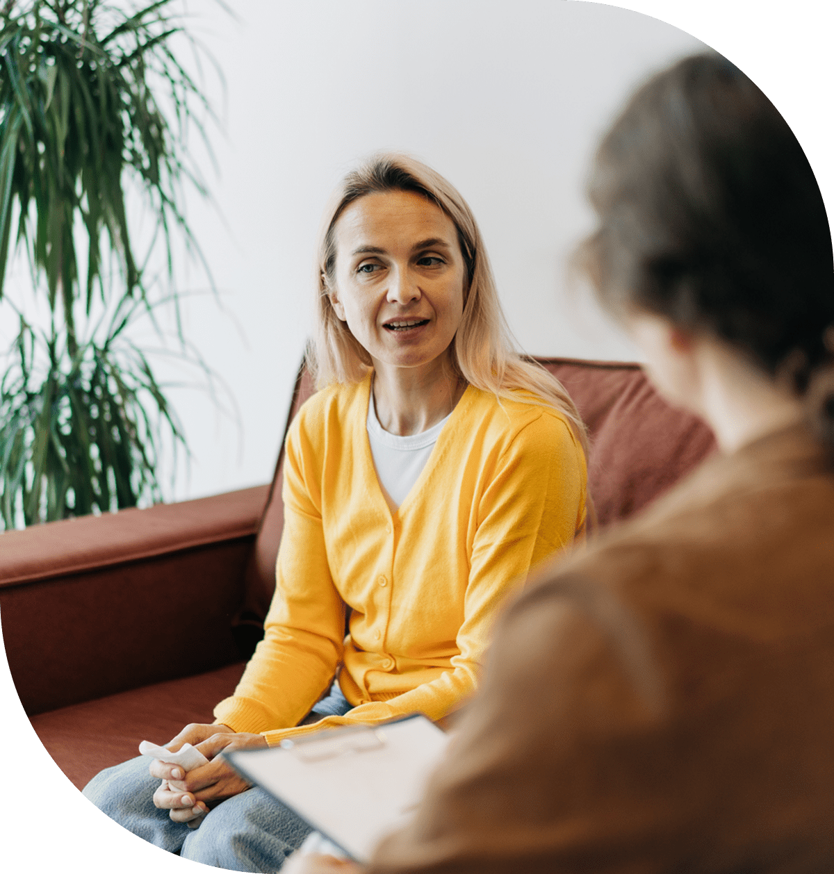 A woman in a yellow sweater talking to another person.