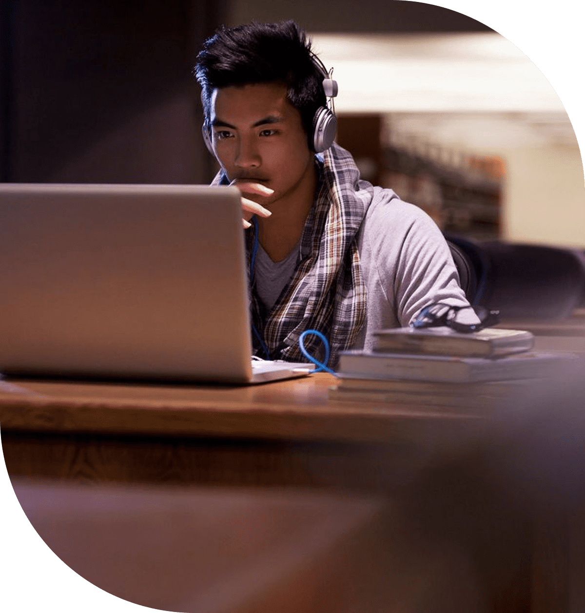 A young man focused on his laptop in a dimly lit room.